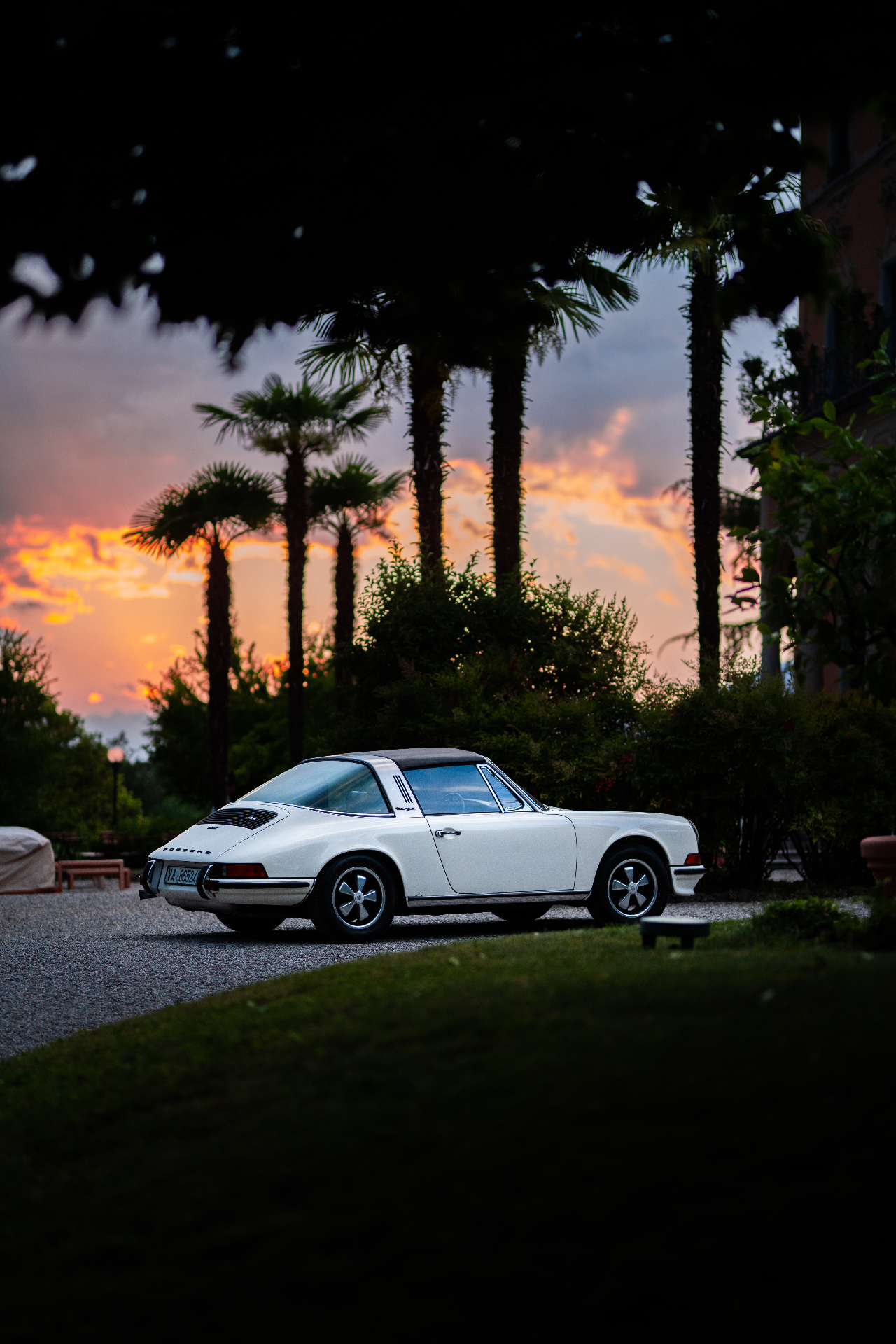 Porsche bianca al tramonto tra le palme davanti alla villa